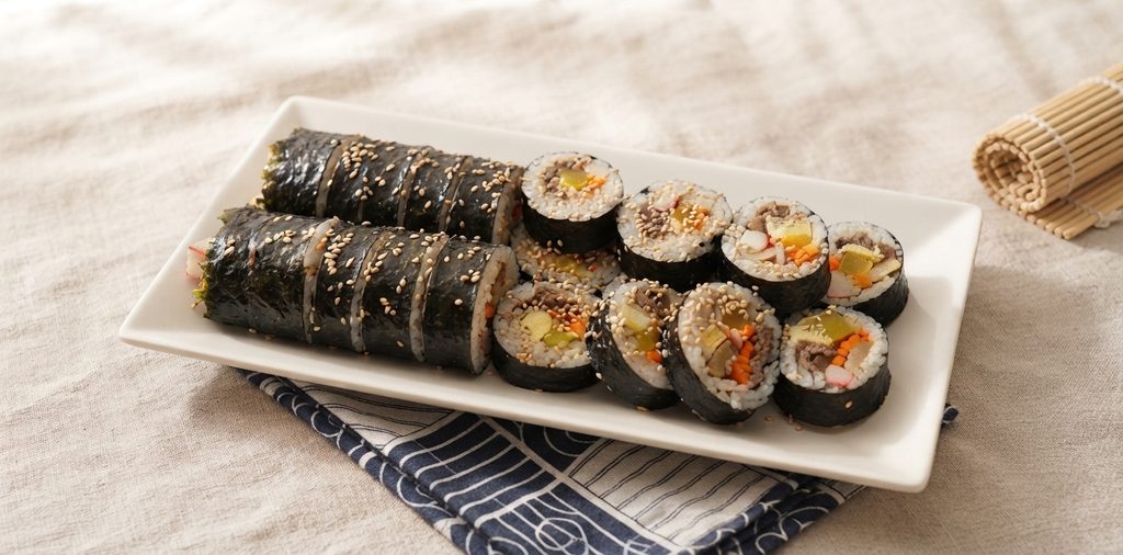 Sliced kimbap rolls arranged on a wooden board with visible egg, carrot, and beef filling